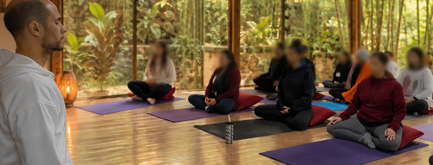 Grupo em meditação silenciosa em um salão de madeira cercado por natureza